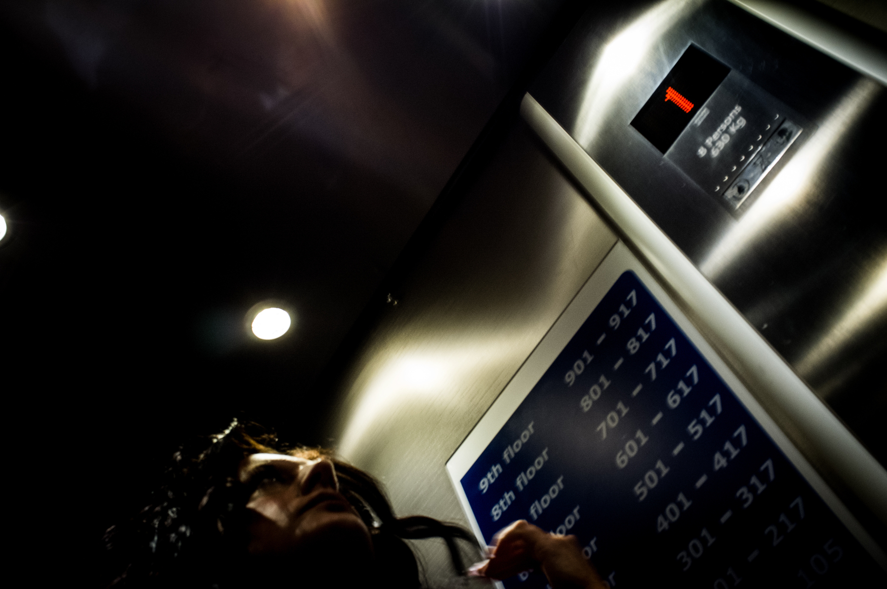 A photo shot from the hip of a woman standing inside an elevator, with lit buttons and floor numbering visible.