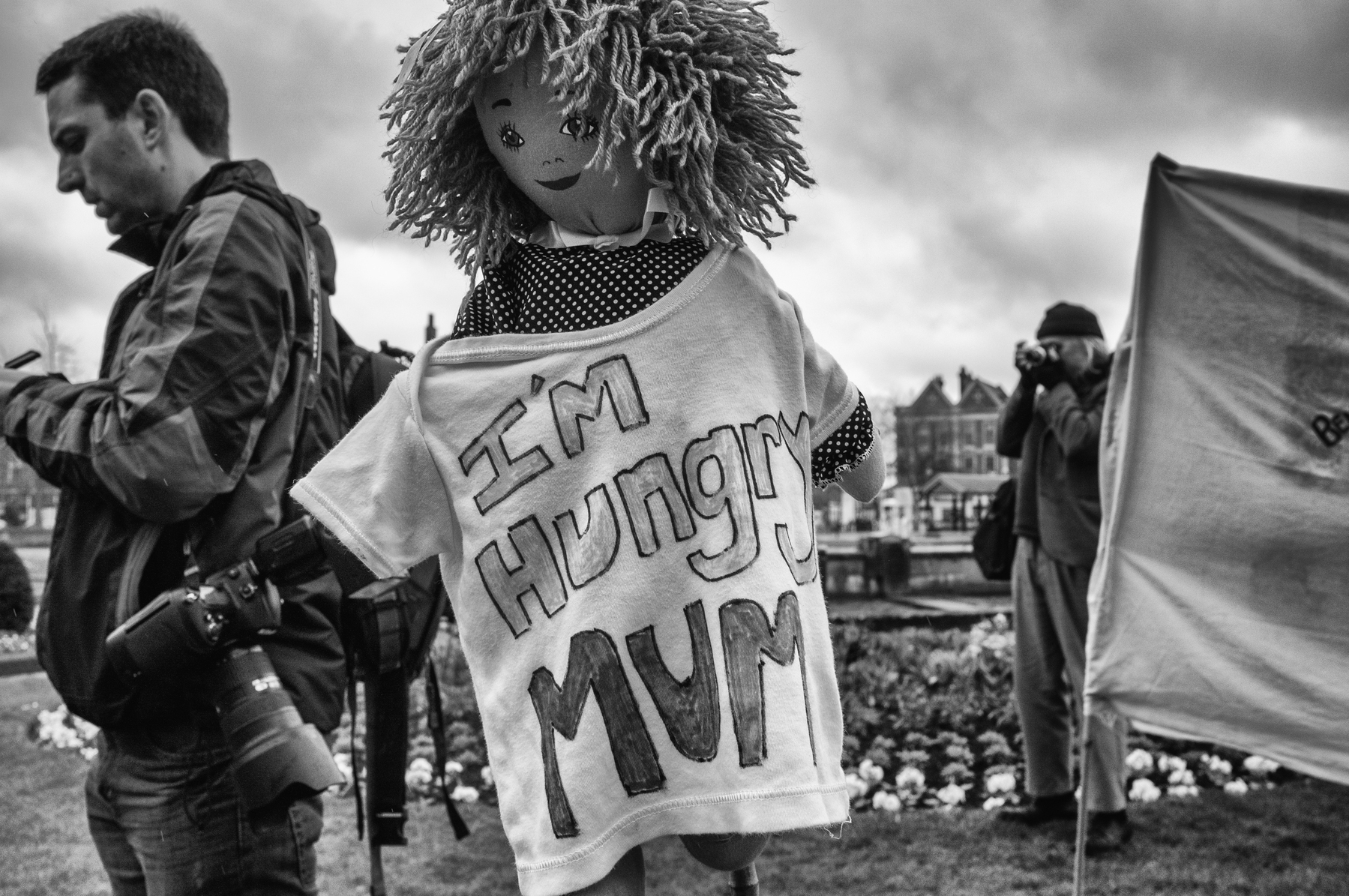 A doll's body is propped onto a pole, wearing a shirt saying I'm Hungry Mum during a protest in the city of Hull.  In the background photographers are capturing the scene.