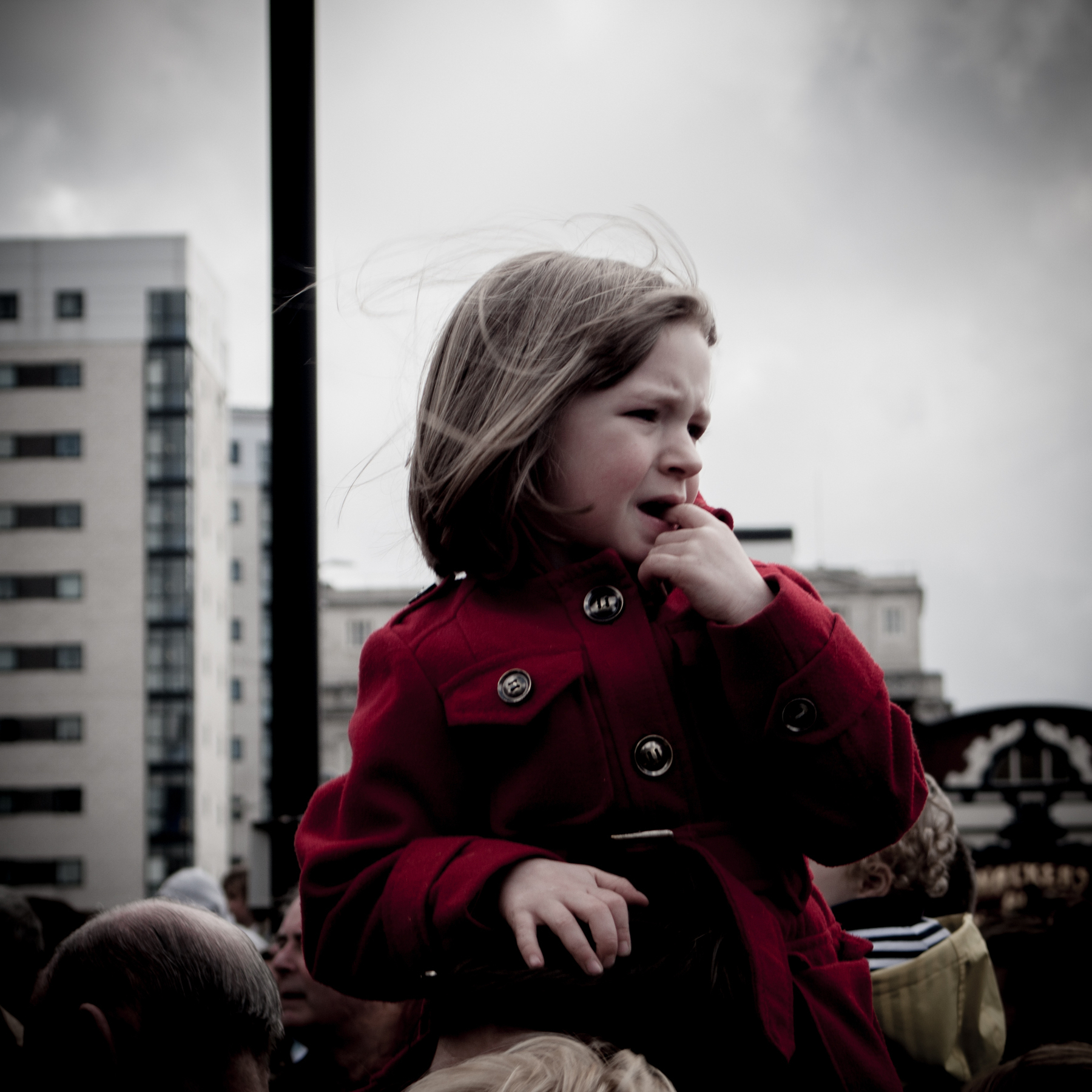 Auto-generated description: A young child in a red coat is being carried above a crowd in Liverpool city centre.