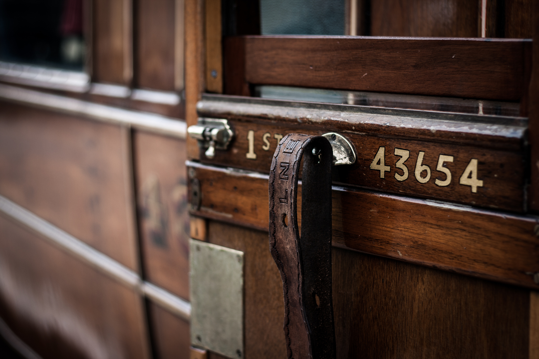 Auto-generated description: A close-up of a wooden train carriage door displays the numbers 43654 and the label 1ST, along with a leather handle.