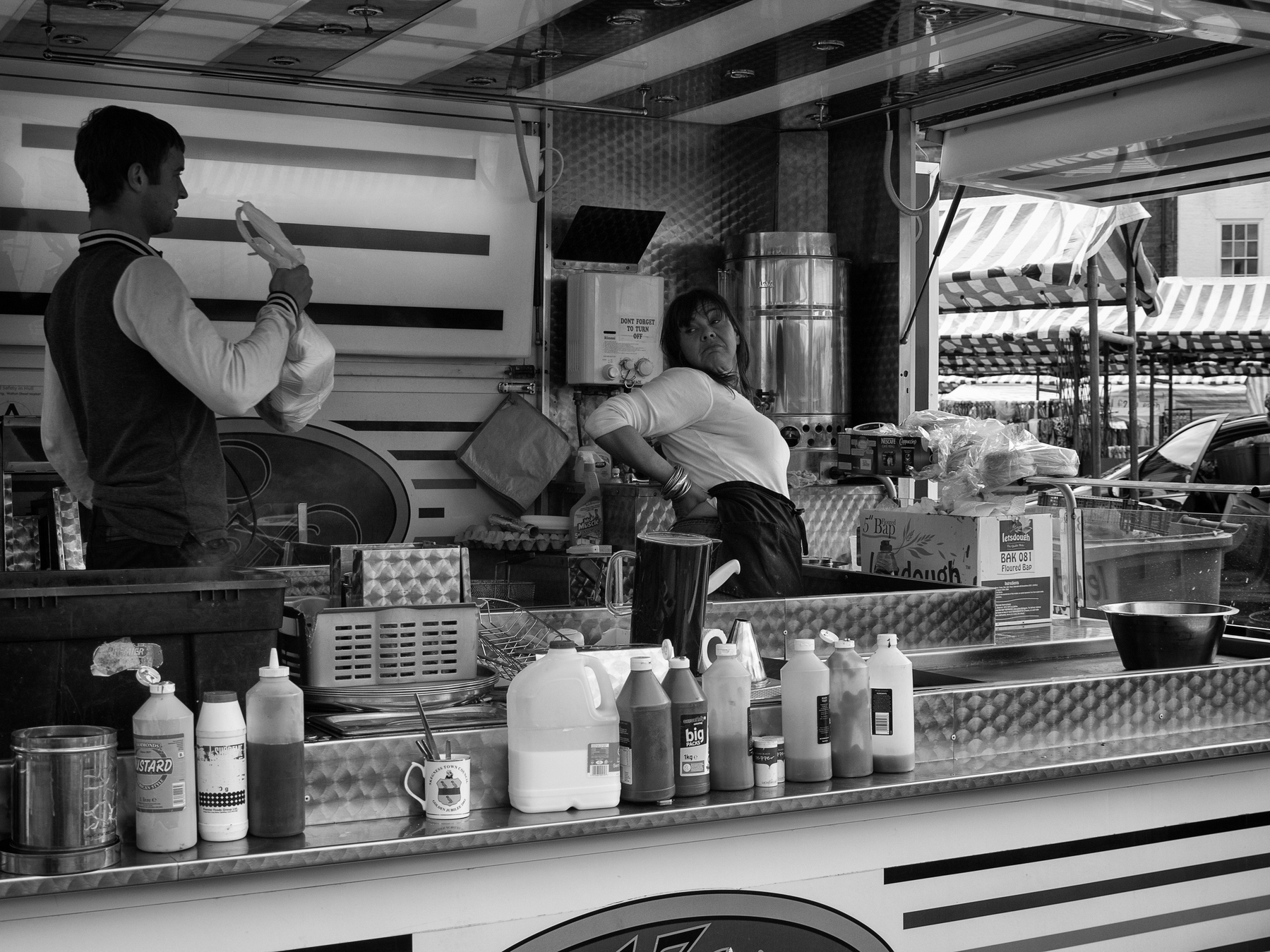 Auto-generated description: A man and woman are working at a food stall filled with various condiments and supplies.